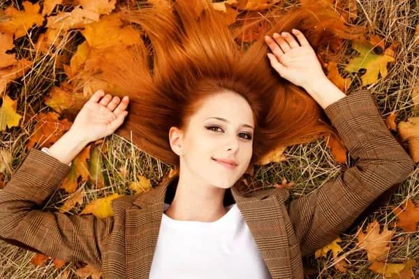 Femme aux cheveux roux allongée dans les feuilles d'automne