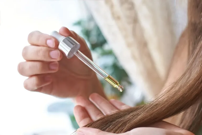 Gros plan sur une main utilisant une pipette pour déposer de l'huile capillaire sur des cheveux longs et brillants.