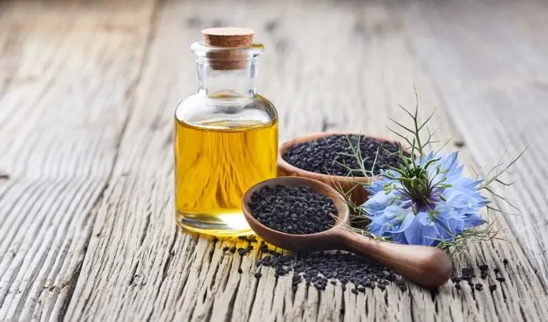 Bol rempli de graines de nigelle à côté d’une fiole d’huile sur une table en bois, accompagné de lavande séchée