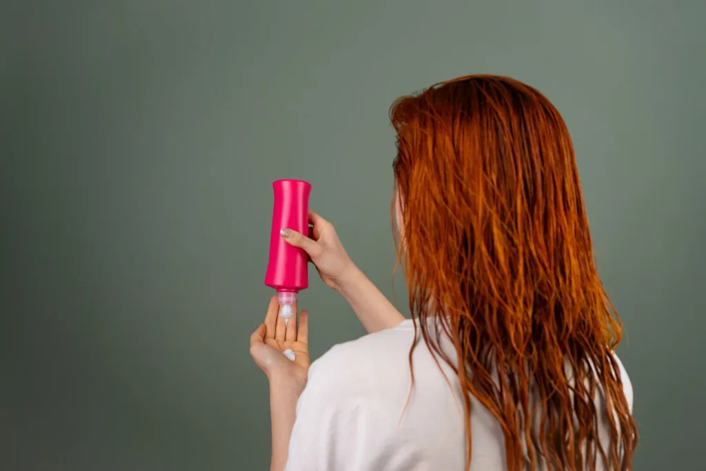 Femme aux cheveux roux mouillés qui applique un après-shampoing