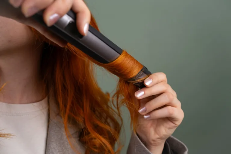 Femme bouclant ses longs cheveux roux avec un appareil chauffant