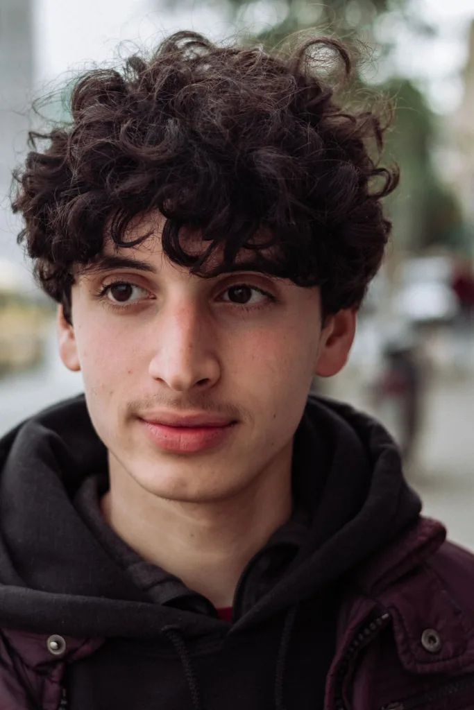 Jeune homme aux boucles mi-longues laissées naturelles