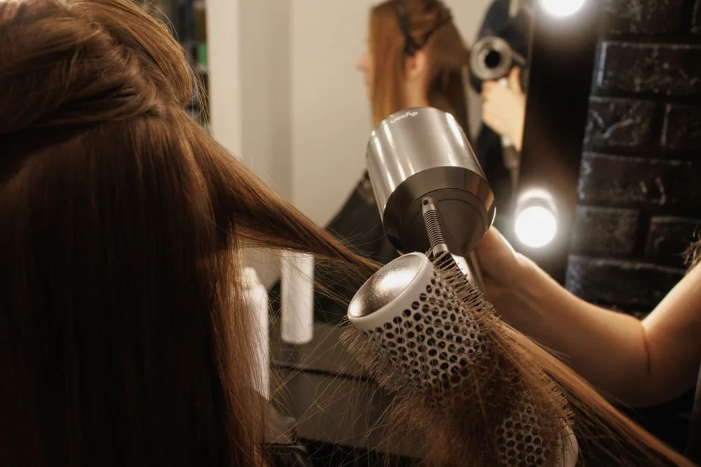 Coiffeuse qui fait un brushing avec une brosse ronde et un sèche-cheveux