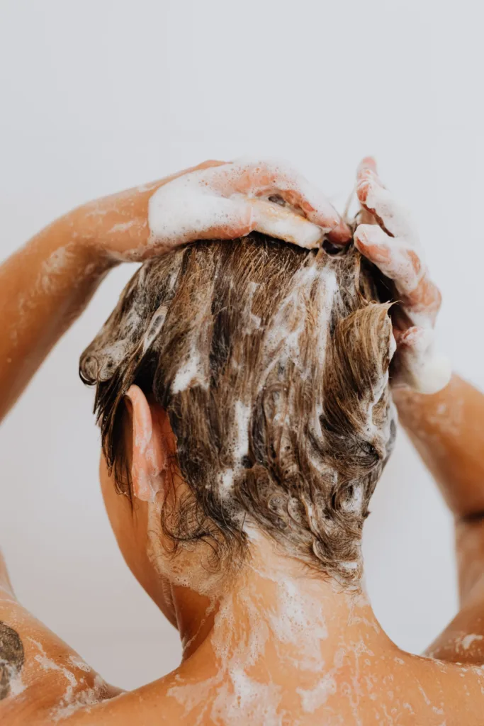 Femme qui masse un shampoing moussant sur son cuir chevelu sous la douche