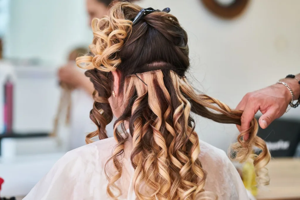 Coiffeuse qui crée des boucles au fer sur cheveux longs blonds