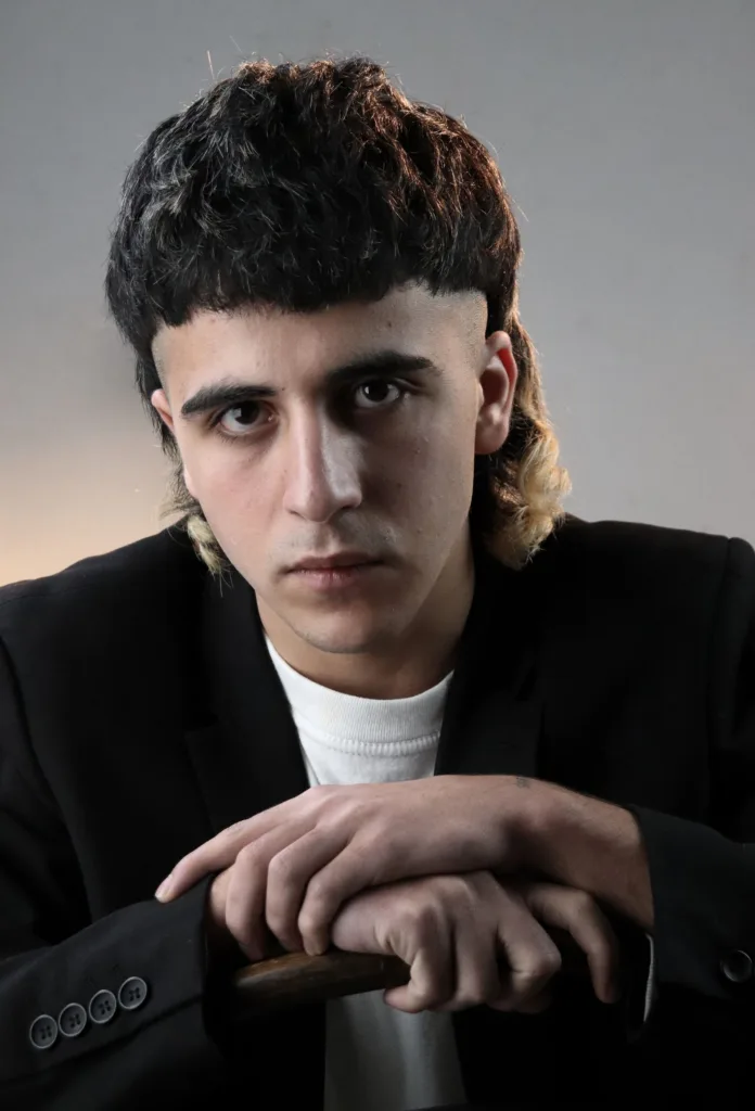 Jeune homme avec un mulet moderne : boucles sur le dessus, nuque plus longue