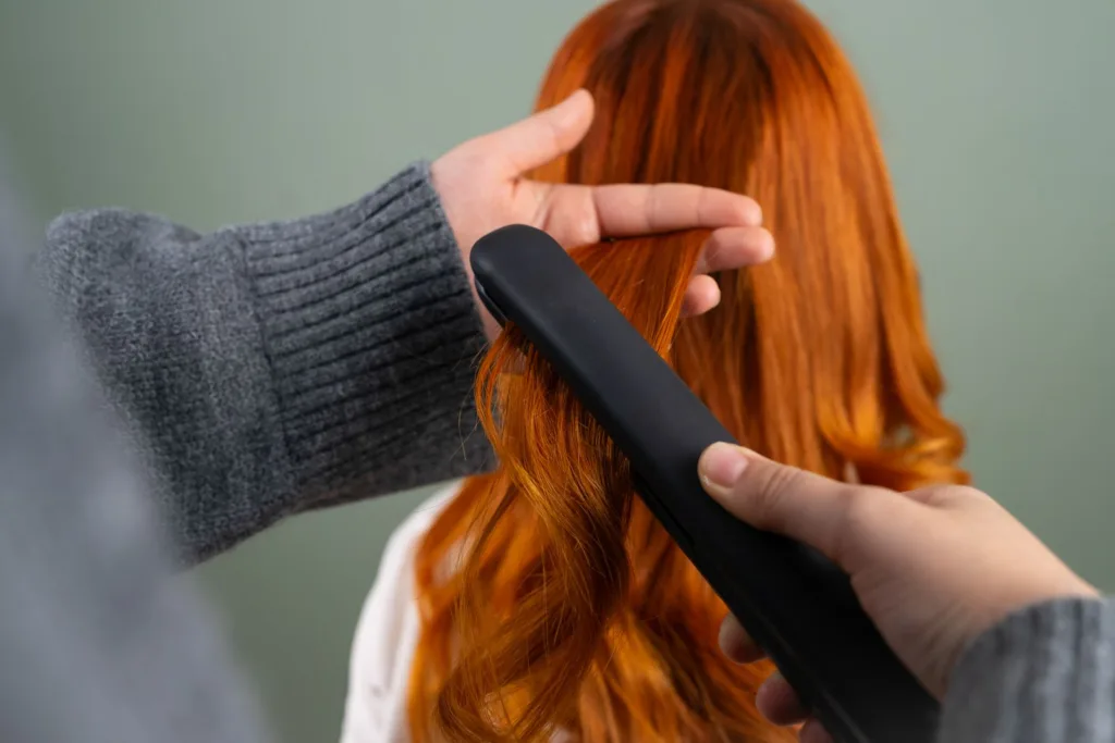 Mains lissant de longs cheveux roux au fer à lisser
