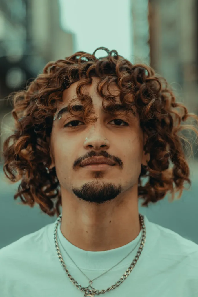 Jeune homme aux cheveux bouclés mi-longs, dégradé léger sur les côtés