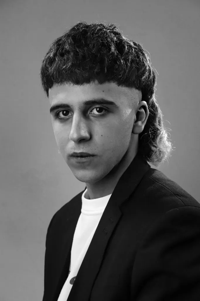 Homme avec un mulet bouclé : boucles sur le dessus, côtés courts et nuque longue, noir et blanc