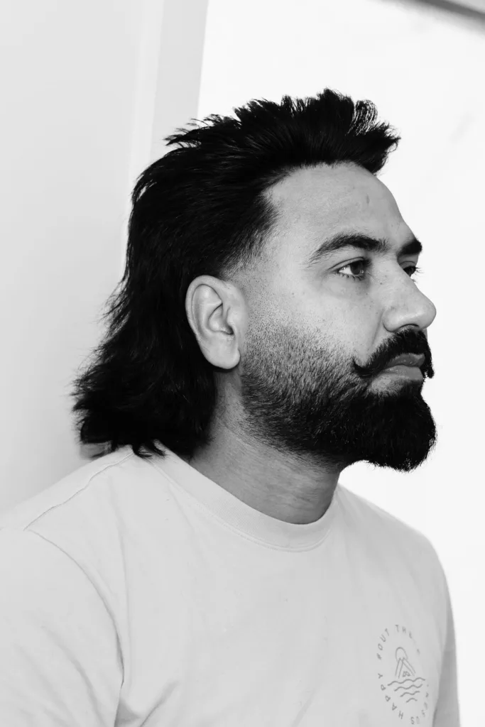 Homme barbu de profil avec un mulet classique : côtés coupés sans dégradé, nuque longue jusqu'aux épaules, noir et blanc