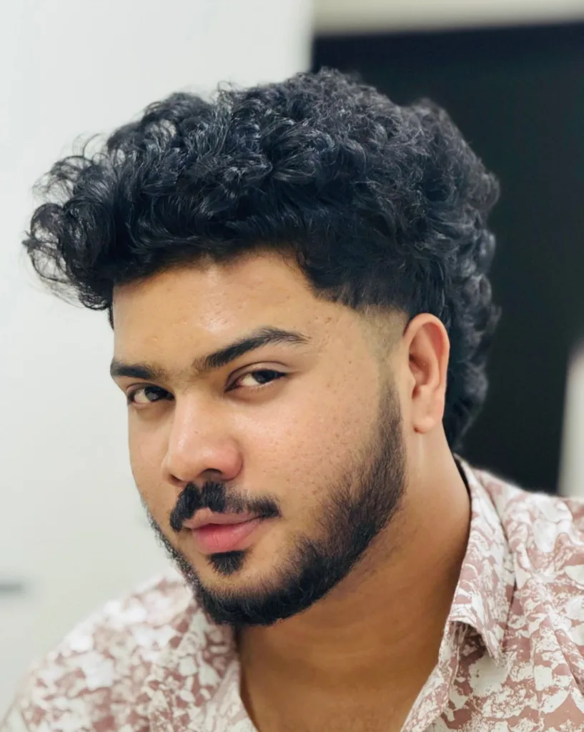 Homme avec un mulet espagnol : dessus bouclé volumineux, tempes dégradées au contour net, boucles dans la nuque