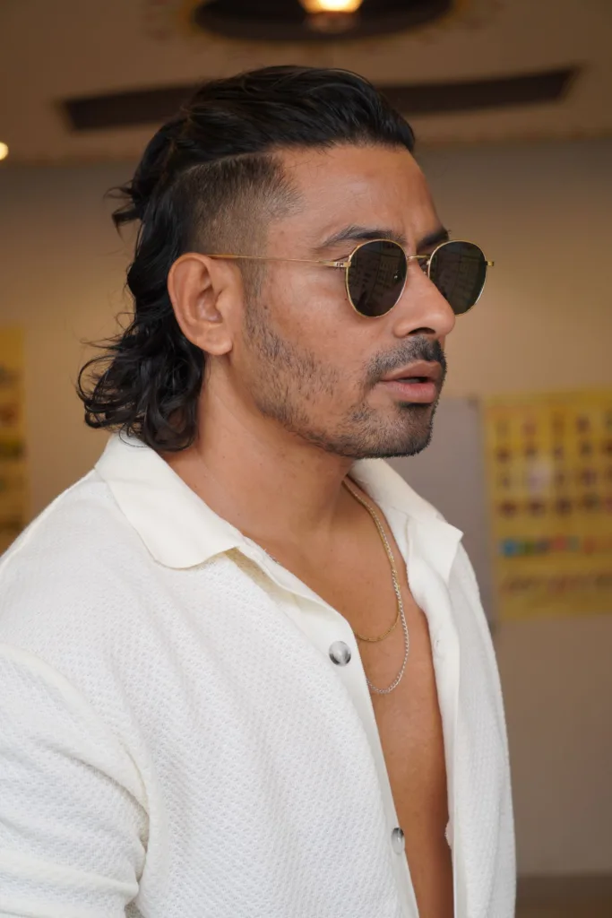 Homme de profil avec un taper mullet : côtés dégradés courts, dessus coiffé en arrière, nuque longue et ondulée