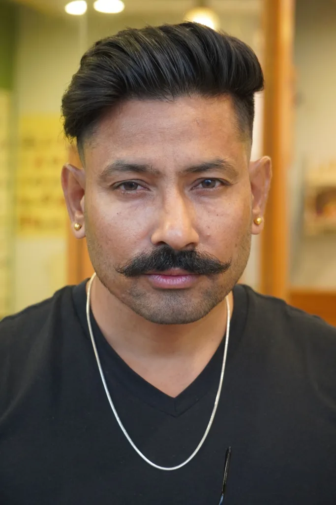 Homme à moustache avec un pompadour : dessus volumineux ramené vers l'arrière, côtés courts