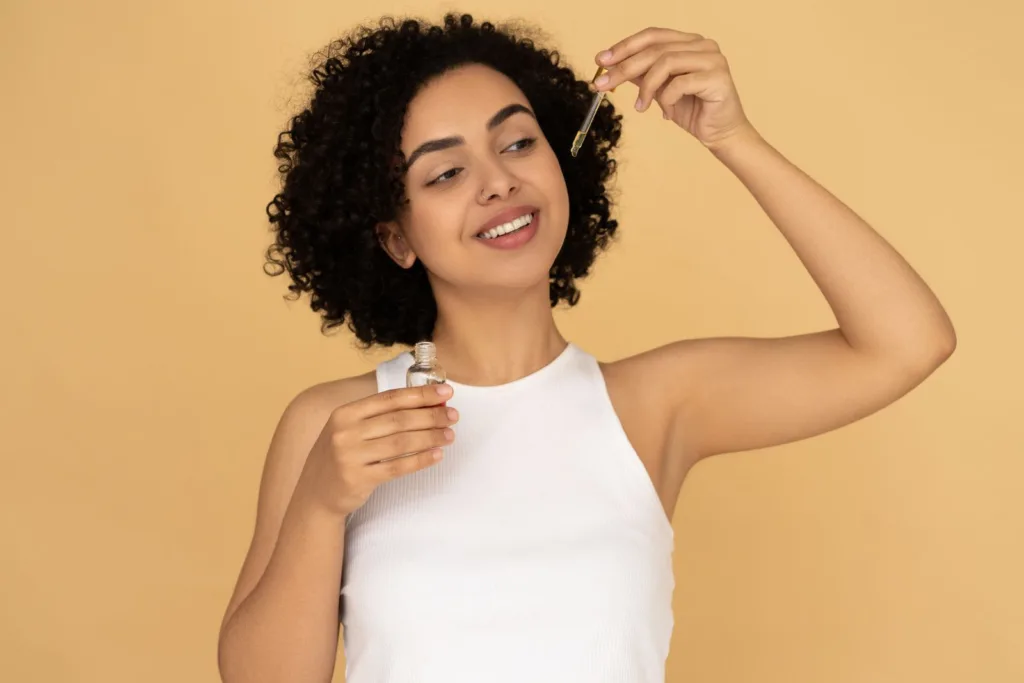 Femme aux cheveux bouclés appliquant un soin avec une pipette